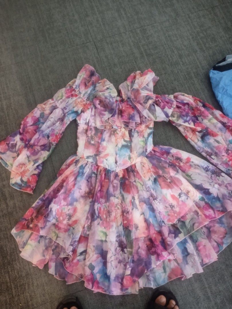 Floral Ruffle Off-Shoulder Mini Dress (Category: Dresses) located in Cebu City. Submitted by newbeethrift (Listing ID 1464861924, Image 1). Description: - Style: Off-shoulder floral chiffon dress - Colors: Multi-colored with pink, purple, and blue tones - Details: Dramatic ruffled trim, long bishop sleeves with flared cuffs - Fit: Fitted bodice with a flared, layered high-low skirt - Material: Lightweight, flowy, and fully patterned - Condition: 