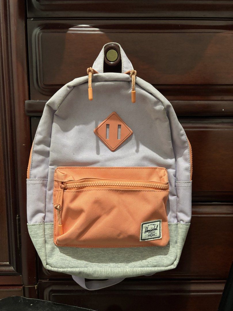 Herschel Supply Co. Heritage Kids Backpack Multi-color (Category: Backpacks) located in Manila. Submitted by amphitrite_ (Listing ID 1464780639, Image 2). Description: - Brand: Herschel Supply Co. - Colorway: Lavender, orange, and grey - Exterior: Front zippered pocket, iconic logo patch, and stylish leather diamond accent - Interior: Signature red and white striped lining with a built-in name label slot - Comfort: Padded, adjustable shoulder str