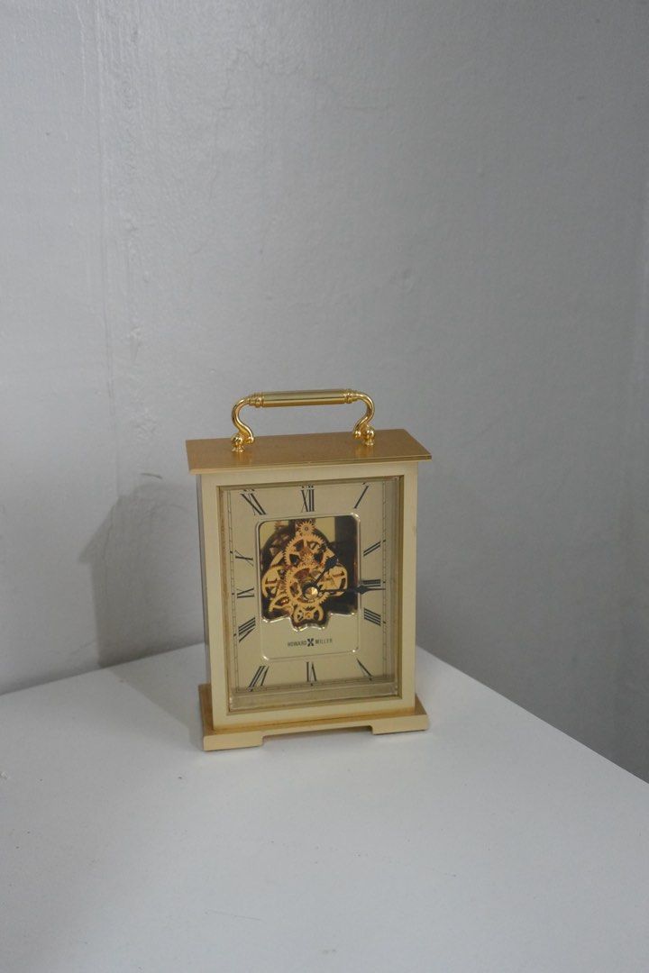 Howard Miller Skeleton Dial Carriage Tabletop Clock (Category: Clocks) located in Manila. Submitted by shopfilipina1993 (Listing ID 1464883014, Image 1). Description: - Brand: Howard Miller - Finish: gold tone with a clean polished look - Dial: Classic Roman numerals and eye-catching visible gear skeleton design - Design: Rectangular metal case, top carrying handle, flat base, and clear glass front panel - Power: Battery-operated movement - Place