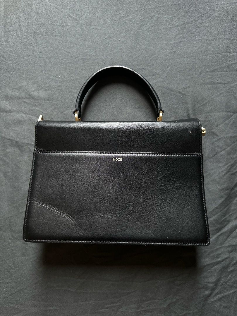 HOZE Black Leather Top Handle Handbag (Category: Tote Bags) located in Manila. Submitted by shopwmsl123 (Listing ID 1464786334, Image 3). Description: - Brand: HOZE - Color: Black with gold-tone hardware - Style: Structured minimalist handbag with top handle - Design: Accordion-style gusset and flap closure with front gold emblem - Compartments: Multiple inside compartments plus a back pocket with brand stamp - Condition: Clean exterior and inter