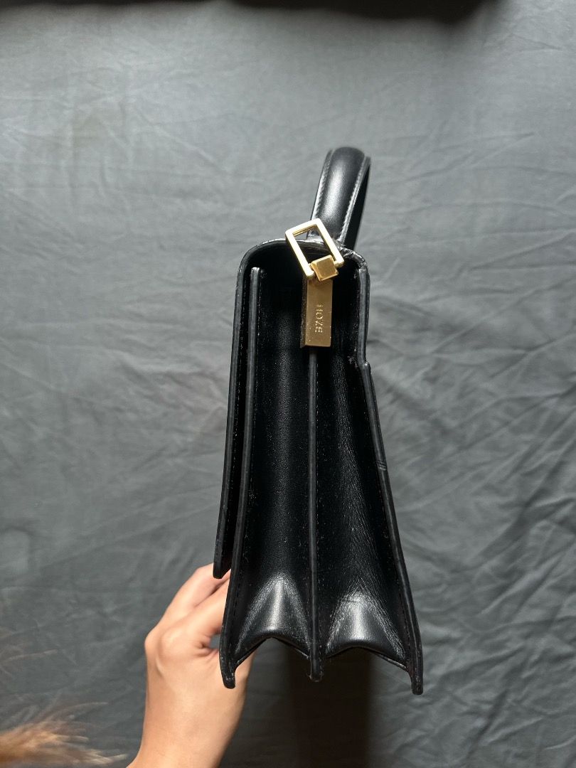 HOZE Black Leather Top Handle Handbag (Category: Tote Bags) located in Manila. Submitted by shopwmsl123 (Listing ID 1464786334, Image 2). Description: - Brand: HOZE - Color: Black with gold-tone hardware - Style: Structured minimalist handbag with top handle - Design: Accordion-style gusset and flap closure with front gold emblem - Compartments: Multiple inside compartments plus a back pocket with brand stamp - Condition: Clean exterior and inter
