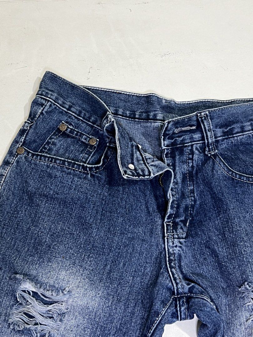 Jagthug Ripped Blue Denim Jeans (Category: Jeans) located in Manila. Submitted by sennisen (Listing ID 1464924901, Image 2). Description: - Brand: Jagthug - Style: Blue denim jeans with heavy distress and ripped details - Wash: Dark wash with intentional fading on the thighs - Features: Frayed hems, classic button fly closure, metal hardware, and standard pockets - Details: Red brand label stitched near the waistband - Condition: Excellent, trend