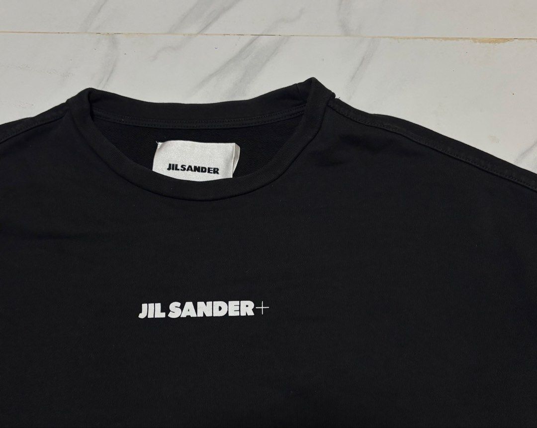 Jil Sander+ Black Logo Sweatshirt (Category: Coats, Jackets and Outerwear) located in Baguio. Submitted by thriftedbaguio (Listing ID 1464831635, Image 2). Description: Excellent Condition Size Large Tagged Dimensions 25*25 Color rate 10 - Brand: Jil Sander+ - Color: Black - Material: 100% heavy cotton - Origin: Made in Italy - Design: Classic crewneck with subtle white chest logo - Details: Ribbed cuffs and hem - Condition: Clean, premium piece.