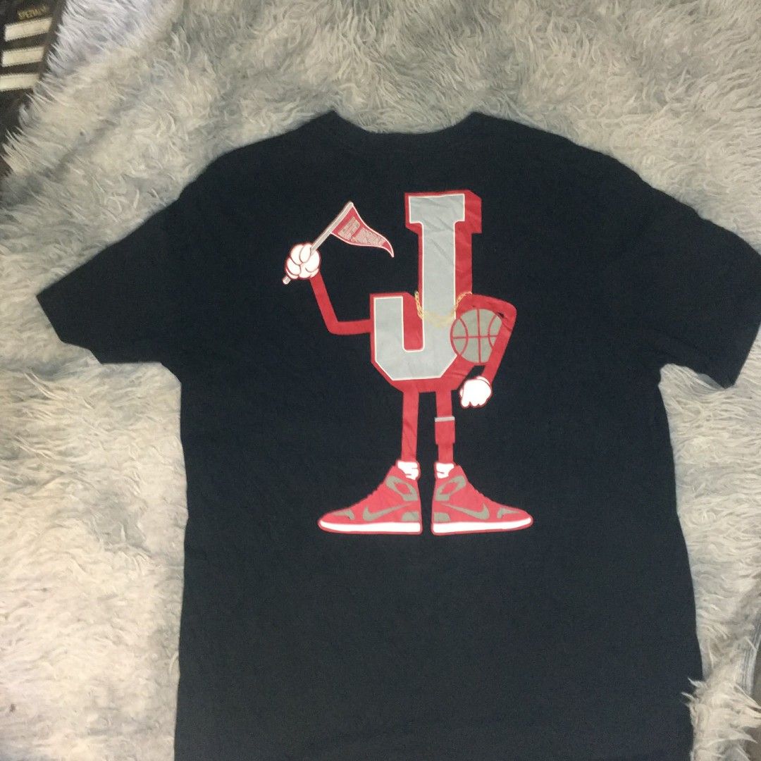 Jordan Black Graphic Tee (Category: Tshirts & Polo Shirts ) located in Manila. Submitted by youngturtle.8e129a (Listing ID 1464966442, Image 3). Description: Black short-sleeve t-shirt from Jordan. Small pennant logo on the chest, red Jumpman silhouette on the left sleeve. Large graphic on the back featuring a cartoon character made of the letter J wearing retro sneakers, holding a pennant and basketball. Ribbed crew neck collar..