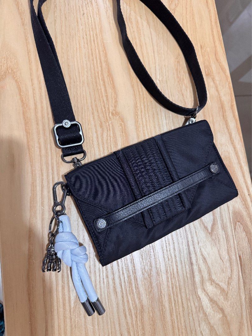 Kipling Black Nylon Crossbody Bag (Category: Cross-body Bags) located in Muntinlupa City. Submitted by mimitatsboutique (Listing ID 1464830774, Image 1). Description: - Brand: Kipling - Color: Black with grey interior lining - Material: Durable nylon - Closure: Envelope foldover flap with magnetic snap - Exterior Features: Pleated front pocket, vertical leather strap detail, and iconic metallic monkey keychain with light blue cord - Interior Feat
