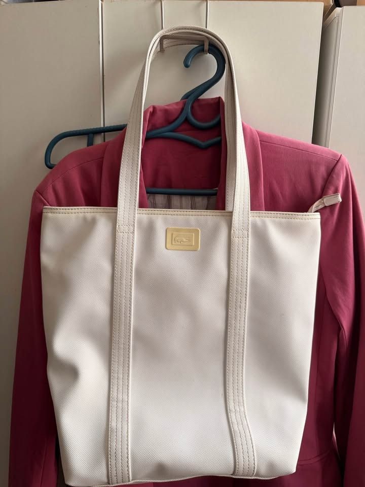 Lacoste Off-White Canvas Tote Bag Vertical (Category: Tote Bags) located in Caloocan City. Submitted by clemg6 (Listing ID 1464784273, Image 1). Description: - Authentic Lacoste white canvas tote bag - Structured rectangular base with sturdy dual shoulder straps - Secure zip top closure - Vibrant yellow interior lining with a leather Lacoste brand patch - Clean exterior fabric showing minimal wear - Perfect for daily use or casual outings 15x13x4
