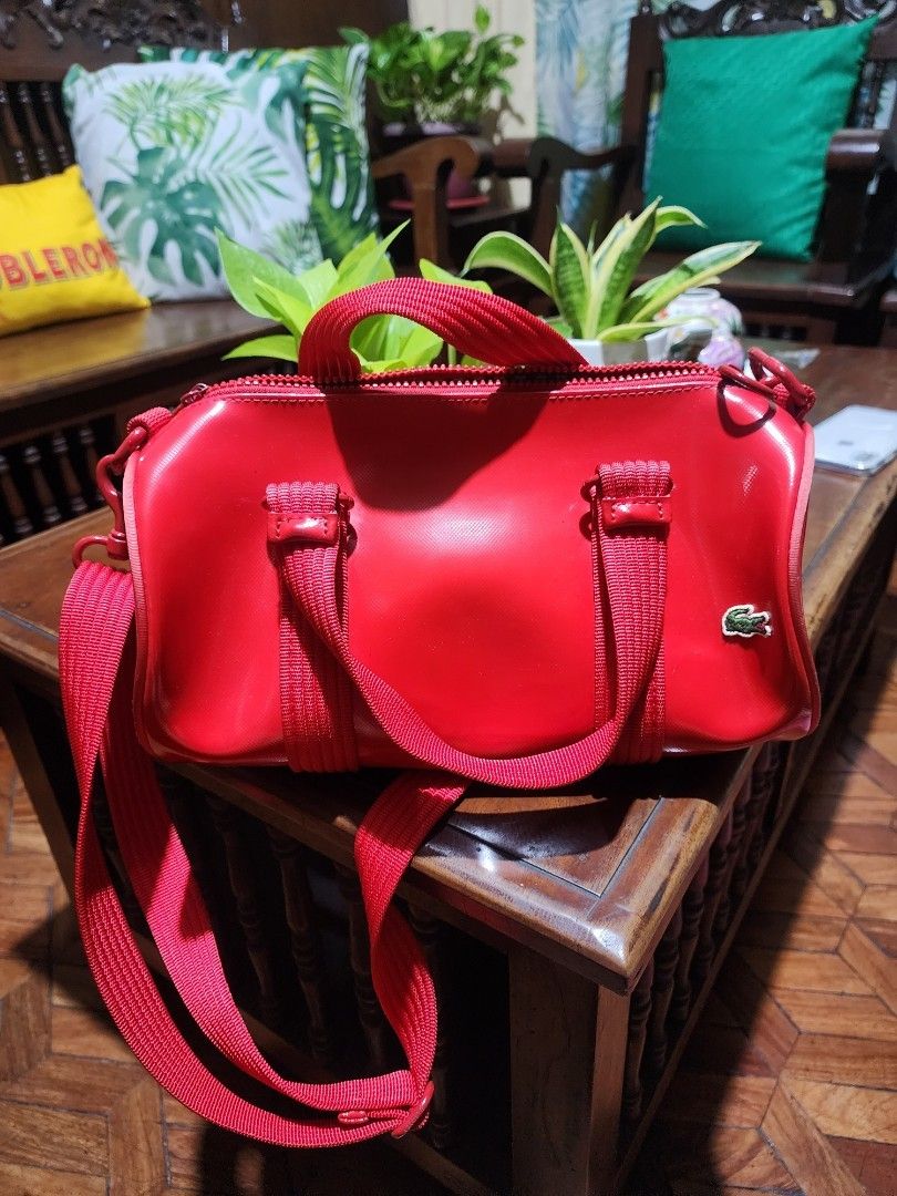 Lacoste Red Vinyl Crossbody Bag (Category: Cross-body Bags) located in Dasmarinas. Submitted by my_preloved_kabinet (Listing ID 1464814967, Image 3). Description: - Brand: Lacoste - Material: Glossy vinyl in vibrant red - Features: Dual red webbed handles, matching detachable shoulder strap with metal clasps, iconic green crocodile logo patch - Interior: Green and white striped fabric lining with a secure zipper closure and round Lacoste pull - C