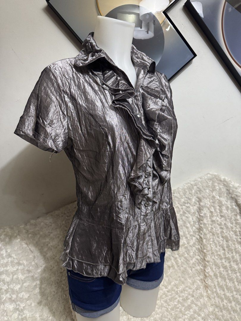 Metallic Silver Ruffle Short Sleeve Blouse (Category: Blouses) located in Marikina City. Submitted by lorradel (Listing ID 1464898312, Image 2). Description: - M on tag fits up to Large - Metallic silver short sleeve blouse with a unique crinkled texture - Features a button-up front with dramatic ruffles along the placket and collar - Flared hem provides a flattering and stylish shape - Lightweight material with a subtle, elegant sheen - Versatil