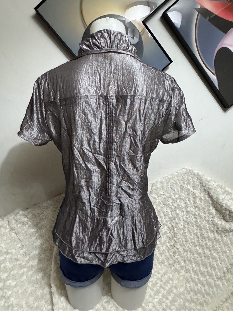 Metallic Silver Ruffle Short Sleeve Blouse (Category: Blouses) located in Marikina City. Submitted by lorradel (Listing ID 1464898312, Image 3). Description: - M on tag fits up to Large - Metallic silver short sleeve blouse with a unique crinkled texture - Features a button-up front with dramatic ruffles along the placket and collar - Flared hem provides a flattering and stylish shape - Lightweight material with a subtle, elegant sheen - Versatil