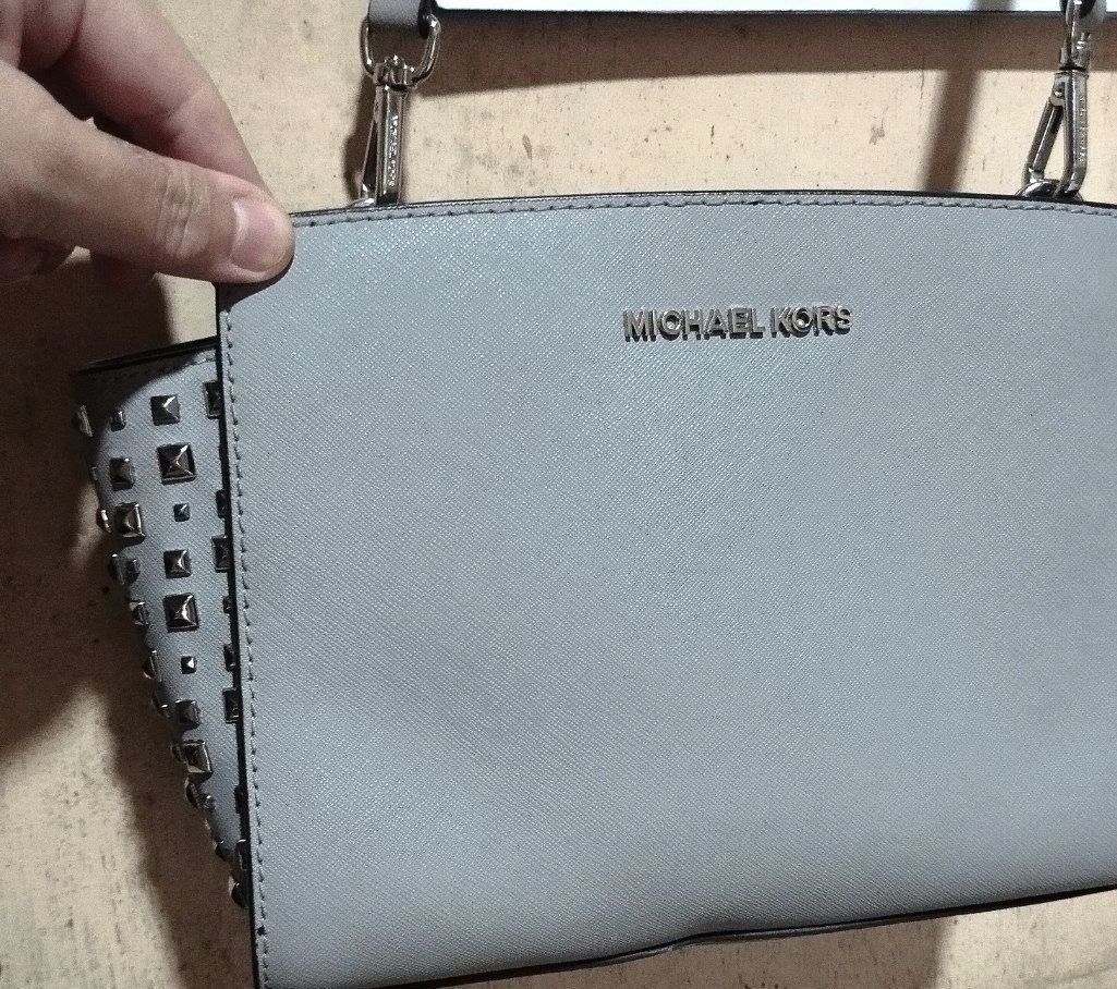 Michael Kors Grey Studded Crossbody Bag (Category: Cross-body Bags) located in Manila. Submitted by lene48 (Listing ID 1464773939, Image 2). Description: - Authentic Michael Kors Crossbody Bag - Color: Light Grey with silver-tone hardware and edgy side studs - Material: Premium Saffiano leather (durable and scratch-resistant) - Strap: Includes adjustable crossbody strap - Interior: Clean fabric lining with MK logo print, 1 zip pocket, and 1 slip 