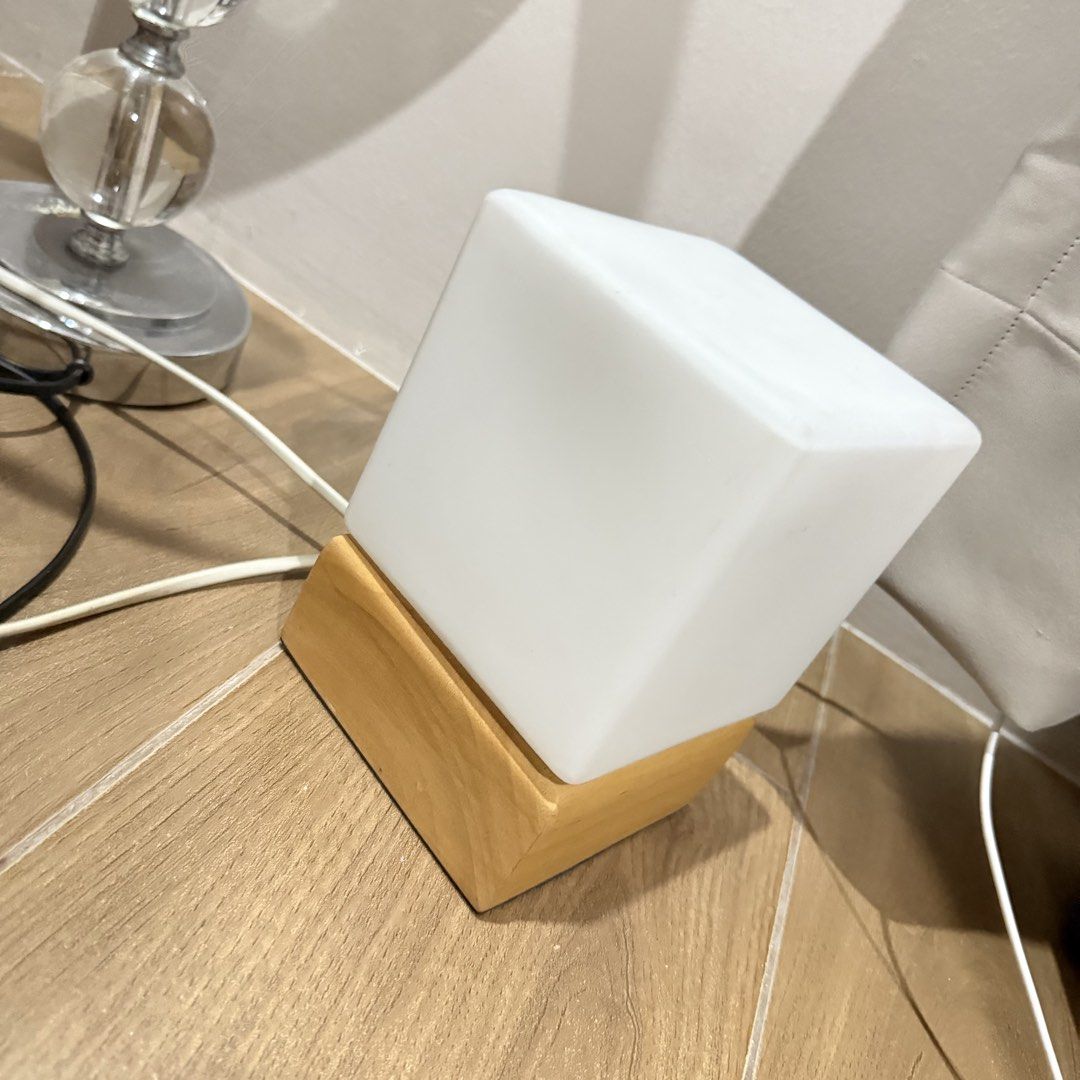 Minimalist cube desk lamp with wooden base (Category: Lighting) located in Marikina City. Submitted by lovegoeson (Listing ID 1464891881, Image 2). Description: - Design: Clean, modern square frosted glass shade with a sturdy wooden base - Lighting: Emits a soft, warm glow ideal for relaxation or work - Placement: Perfect for bedside tables, study desks, or living room accents - Power: Includes a standard plug-in cord for easy setup.