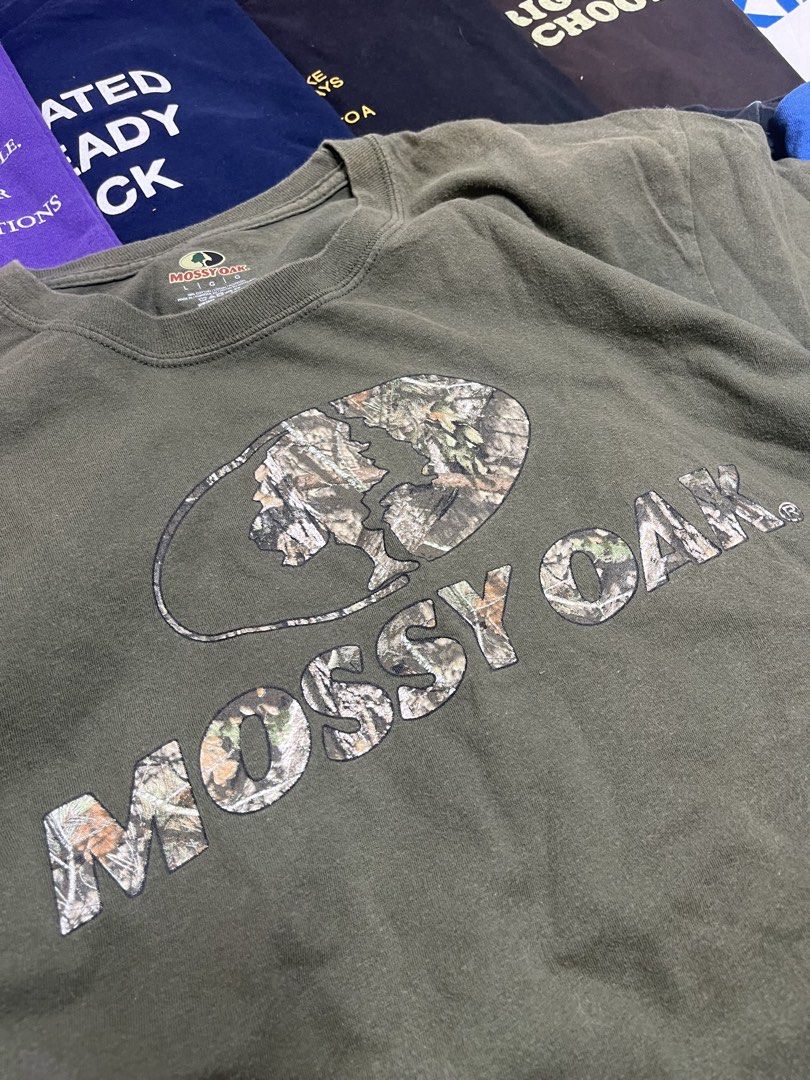 Mossy Oak Green Graphic Tee Size L (Category: Tshirts & Polo Shirts ) located in Baao. Submitted by plainclothesdept (Listing ID 1464785385, Image 2). Description: Mossy Oak width - 22 in. length- 28 in. no flaws - Brand: Mossy Oak - Color: Olive Green - Design: Large chest logo with camo fill and oval border - Material: 100% Cotton (Made in Honduras) - Fit: Standard crew neck, short sleeves - Condition: Clean fabric with minimal fading around th