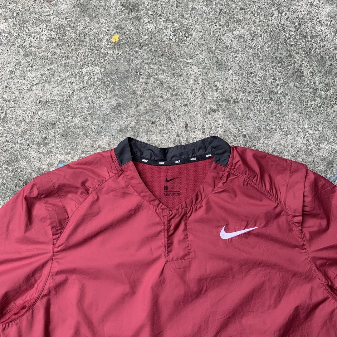 Nike Short Sleeve V-Neck Windbreaker Maroon (Category: Activewear) located in Polangui. Submitted by b0ssl00ts (Listing ID 1464805504, Image 2). Description: - Brand: Nike - Style: Short-sleeve windbreaker - Color: Maroon with dark grey shoulder and cuff panels - Size: Medium - Details: V-neck collar with repeated Nike branding inside, small white Swoosh on left chest - Pockets: Two zippered pockets near the hem with grey pull cords - Origin: Mad