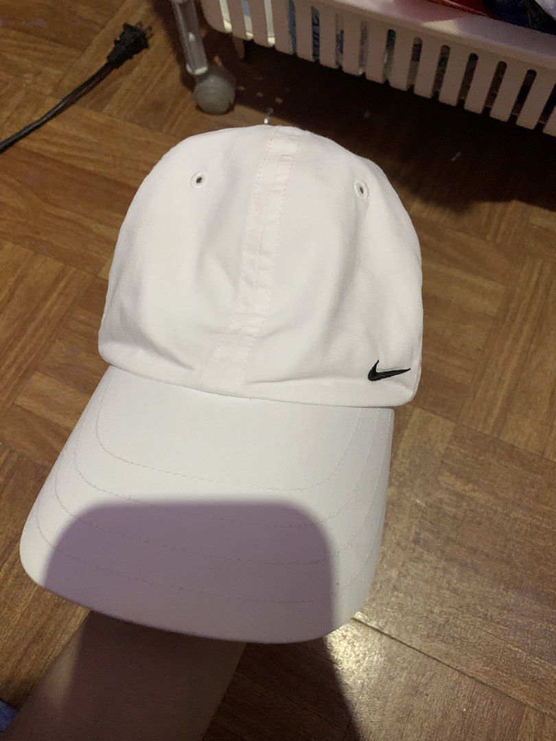 Nike White Baseball Cap (Category: Caps & Hats) located in Manila. Submitted by usagichan_rabbit (Listing ID 1464797702, Image 1). Description: - Brand: Nike - Color: White with black embroidered swoosh logo - Material: 60% cotton, 40% polyester blend - Size: One size fits all with adjustable back strap - Details: Features a small black swoosh on the strap and grey trim underneath the brim - Condition: Inner band shows some discoloration from wea