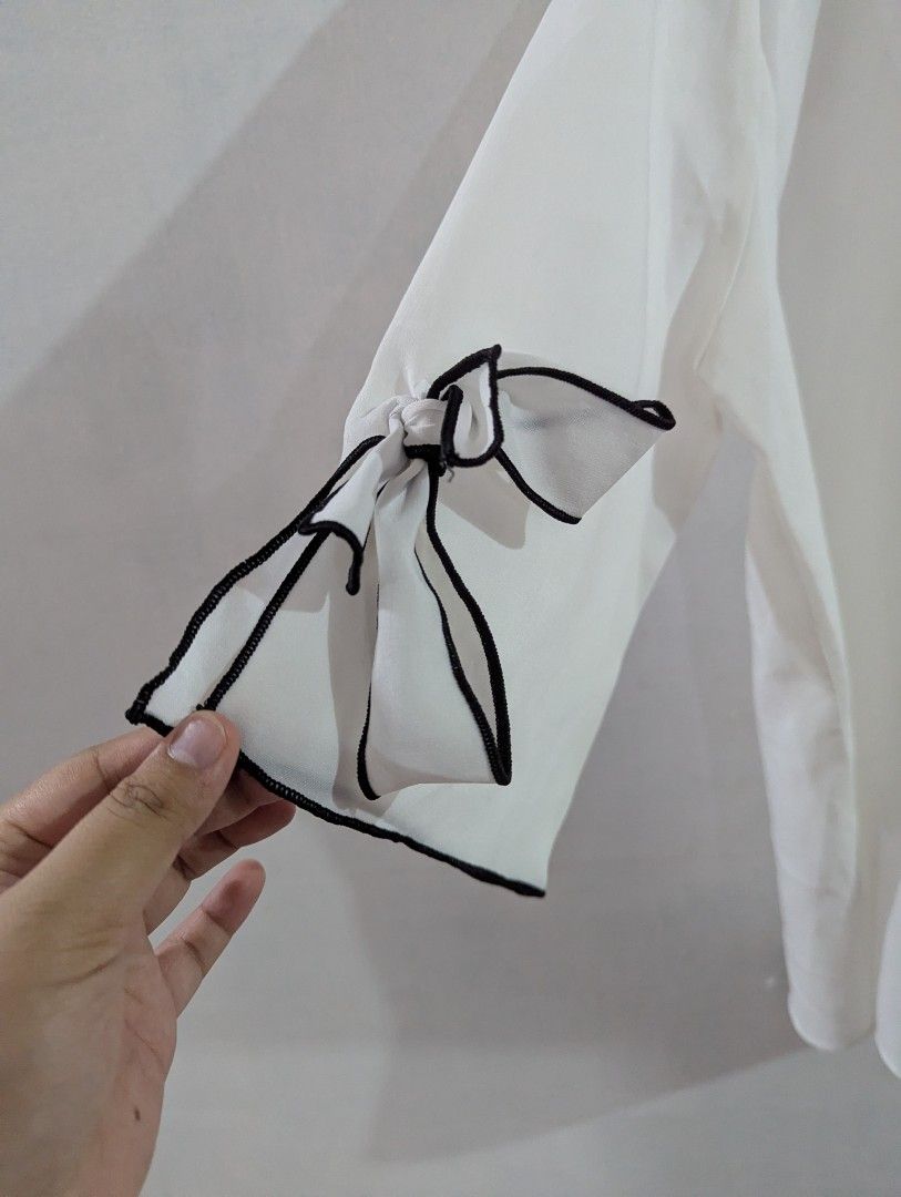 [oppane] O.P.N White Blouse with Black Trim (Category: Blouses) located in Marikina City. Submitted by beybera (Listing ID 1464887865, Image 2). Description: - Brand: oppane O.P.N. (Made in Korea) - Color/Style: White blouse with chic black contrast trim on the round neckline - Details: Short sleeves featuring sweet tied bow accents on both cuffs - Fit: Lightweight, comfortable pullover style - Condition: Clean and well-maintained all around.