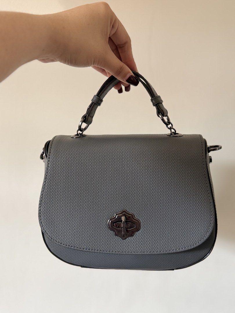Oryany top handle / cross body bag - Dark Grey (Category: Luxury Bags & Wallets) located in Lipa City. Submitted by asleeeh (Listing ID 1464795551, Image 1). Description: Only used once!! Good as new!! Grey handbag with textured pattern. Structured saddle shape with curved bottom edge. Dark gunmetal hardware including distinctive ornate twist lock closure on front flap. Short top handle attached via rings, plus side rings ready for an optional cr