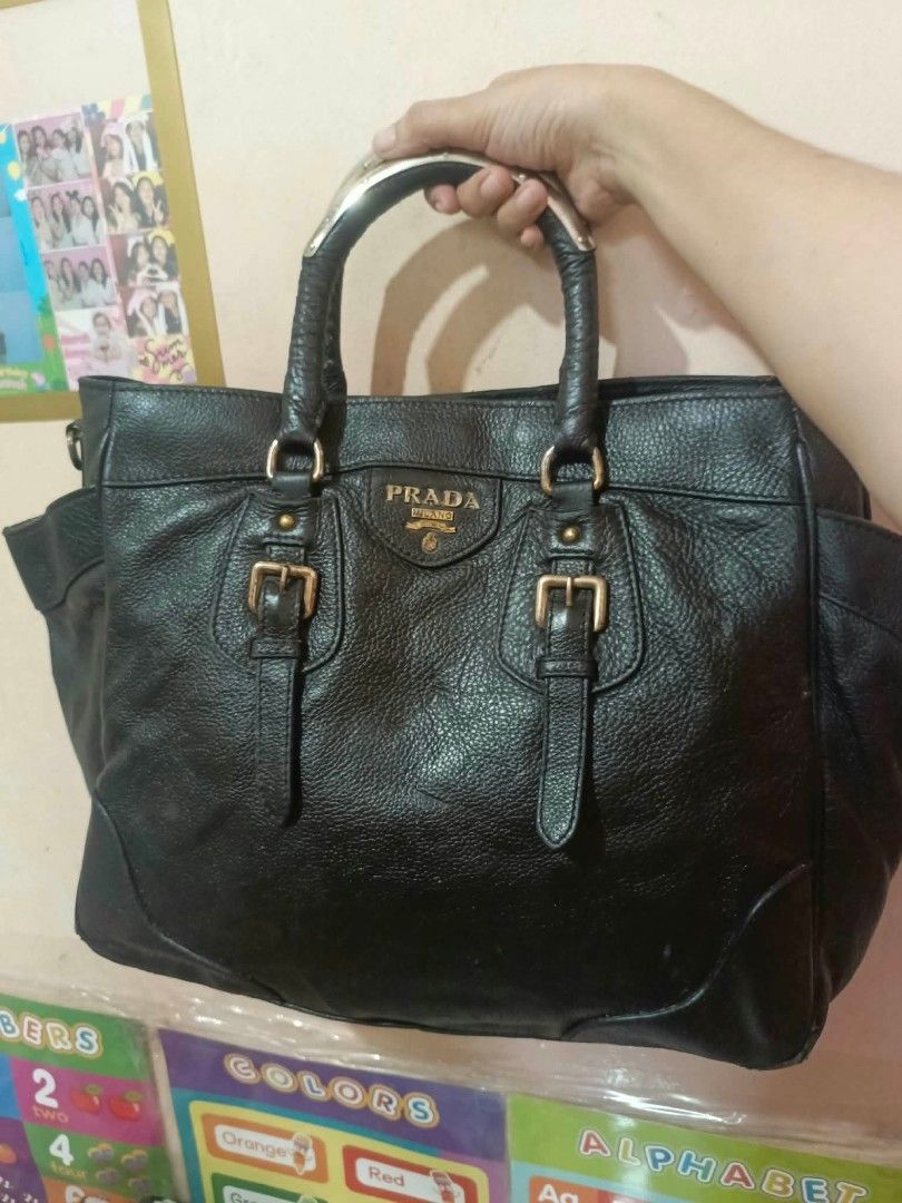 Prada Black Leather Handbag (Category: Luxury Bags & Wallets) located in Manila. Submitted by dei03_diz (Listing ID 1464942750, Image 1). Description: - Authentic black textured leather Prada handbag - Elegant gold-tone hardware and iconic Prada triangle logo - Dual top handles and stylish front buckle straps - Spacious black Prada jacquard fabric interior - Includes an interior zipper pocket and leather logo patch - Perfect, roomy everyday shoul
