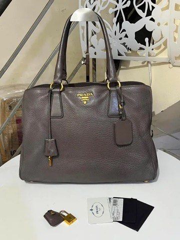 Prada Grey Leather Tote Handbag with Lock and Keys (Category: Tote Bags) located in Quezon City. Submitted by luxuriesbymichiika (Listing ID 1464943926, Image 1). Description: - 100% Authentic Prada pebbled leather tote in a chic dark greyish taupe shade - Spacious interior with secure zip compartments for your daily essentials - Elegant gold-tone hardware and iconic front metal logo lettering - Structured yet soft shape with protective metal fee