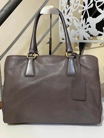 Prada Grey Leather Tote Handbag with Lock and Keys (Category: Tote Bags) located in Quezon City. Submitted by luxuriesbymichiika (Listing ID 1464943926, Image 2). Description: - 100% Authentic Prada pebbled leather tote in a chic dark greyish taupe shade - Spacious interior with secure zip compartments for your daily essentials - Elegant gold-tone hardware and iconic front metal logo lettering - Structured yet soft shape with protective metal fee