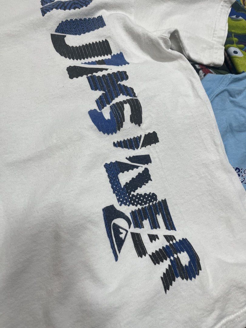 Quiksilver White Vertical Graphic Tee (Category: Tshirts & Polo Shirts ) located in Baao. Submitted by plainclothesdept (Listing ID 1464785380, Image 3). Description: Quicksilver Vertical Spellout width - 17 in. length - 23 in. no flaws - Brand: Quiksilver - Color: White with blue/black graphic - Size: Large - Material: Cotton - Fit: Standard fit - Design: Vertical front print with logo - Style: Vintage surf and skate aesthetic.