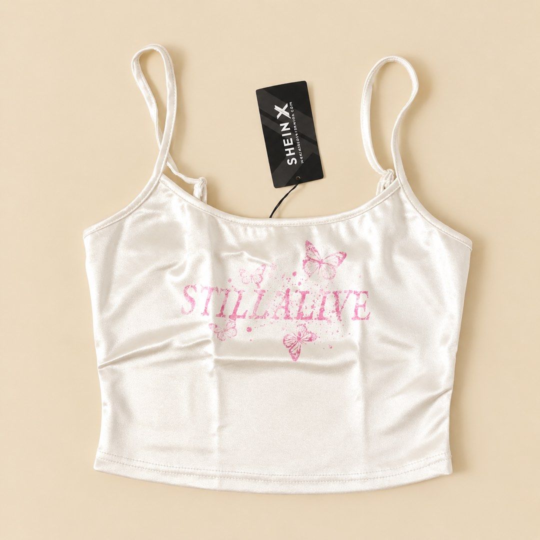 SHEIN X White Satin Butterfly Cami Top (Category: Sleeveless) located in Cavite. Submitted by rareclothing.ph (Listing ID 1464874913, Image 1). Description: SHEIN X White Satin Butterfly Cami Top ‎- White satin cami top from SHEIN X ‎- Features a pink butterfly graphic with 'STILL ALIVE' text ‎- Adjustable spaghetti straps for a perfect fit ‎- Super cute and summery vibe ‎- Ideal for layering or wearing solo .