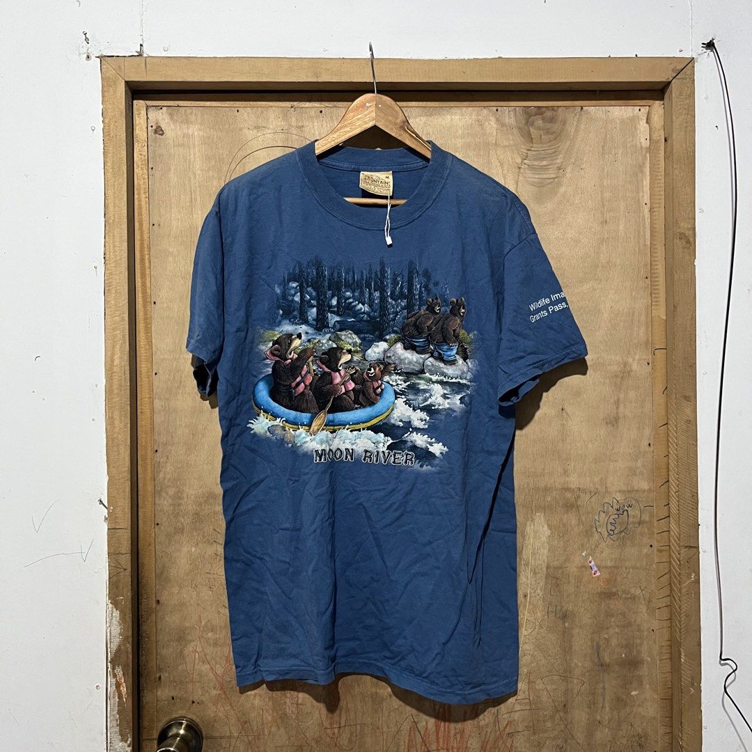 The Mountain Moon River Bear T-Shirt (Category: Tshirts & Polo Shirts ) located in Sipalay. Submitted by rjhndarnie19 (Listing ID 1464795766, Image 1). Description: - Brand: The Mountain - Style: Vintage blue graphic tee with front bear rafting print and 'Moon River' text - Sleeve: Features 'Wildlife Images Grants Pass' text on the left sleeve - Size: Medium - Material: 100% cotton, comfortable fabric with a classic faded look - Origin: Made in U