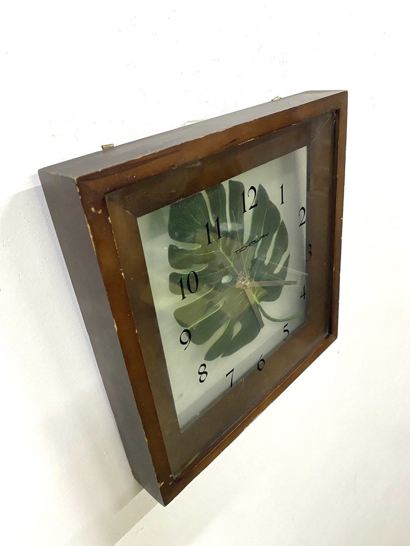 Tickaway Wooden Square Wall Clock with Monstera Leaf Design (Category: Clocks) located in Santa Rosa. Submitted by annie_annie83 (Listing ID 1464874005, Image 3). Description: - Brand: Tickaway - Design: Green Monstera leaf graphic on white background with clear black numbers - Materials: Brown wooden frame with a clear glass front cover - Mechanism: Battery-operated quartz movement - Condition: Good working condition with some scuffs and wear al