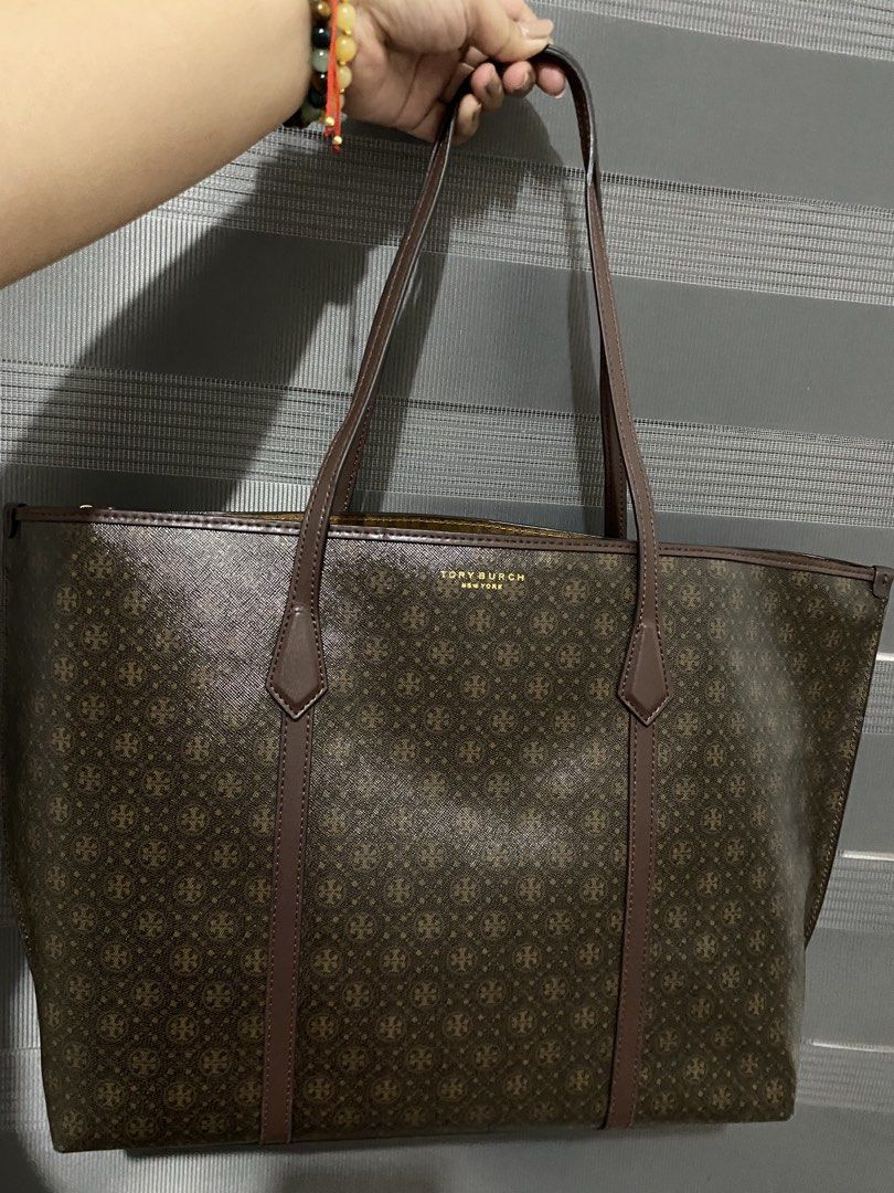 Tory Burch Monogram Tote Bag Brown (Category: Tote Bags) located in Magalang. Submitted by katoenjeru0723 (Listing ID 1464881280, Image 1). Description: - Brand: Tory Burch - Color/Design: Brown monogram print with structured silhouette - Hardware: Gold-tone with protective metal feet at the base - Straps: Dual shoulder straps with brown leather trim - Closure: Secure top zipper - Interior: Custom patterned lining with a convenient snap-flap pock