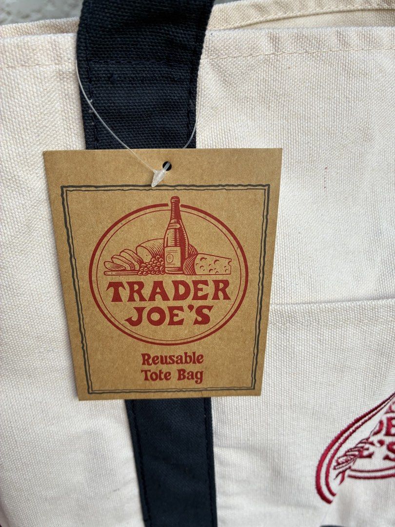 Trader Joe's Reusable Tote Bag (Category: Tote Bags) located in Makati City. Submitted by jeunefille168 (Listing ID 1464774510, Image 2). Description: brand new with tags (never used) Trader Joe's canvas tote bag Size: large 20x14” depth 6” Color: Off-white body with stylish dark blue bottom and matching shoulder straps Features a classic red circular embroidered logo on the front pocket Made from heavy-duty, sturdy cotton construction Spacious i