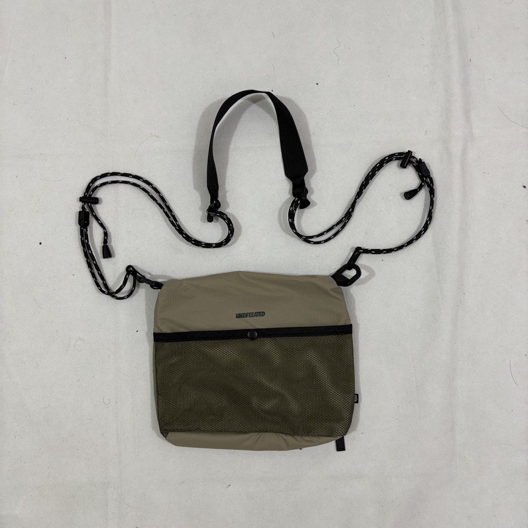 Undefeated Khaki Sling Bag with Mesh Pocket (Category: Sling Bags) located in Cavite. Submitted by itsayaaa (Listing ID 1464836894, Image 1). Description: - Undefeated crossbody bag in khaki and olive green mesh - Lightweight and durable ripstop material - Adjustable black rope shoulder strap with clips for a custom fit - Secure zippered main compartment - Front mesh pocket with snap button closure - Iconic white Undefeated logo printed near the 