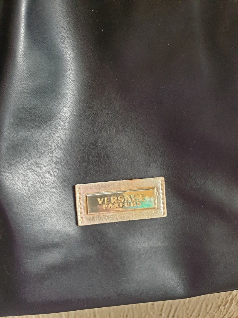 Versace Parfums Black Tote Bag (Category: Tote Bags) located in Las Pinas. Submitted by anggesmart (Listing ID 1464867415, Image 2). Description: - Brand: Versace Parfums - Color: Solid black with elegant gold-tone hardware - Closure: Secure top zip closure - Interior: Fully fabric-lined with a convenient zippered side pocket - Details: Features a chic metallic branded patch on the front - Usage: Spacious main compartment ideal for daily essentia