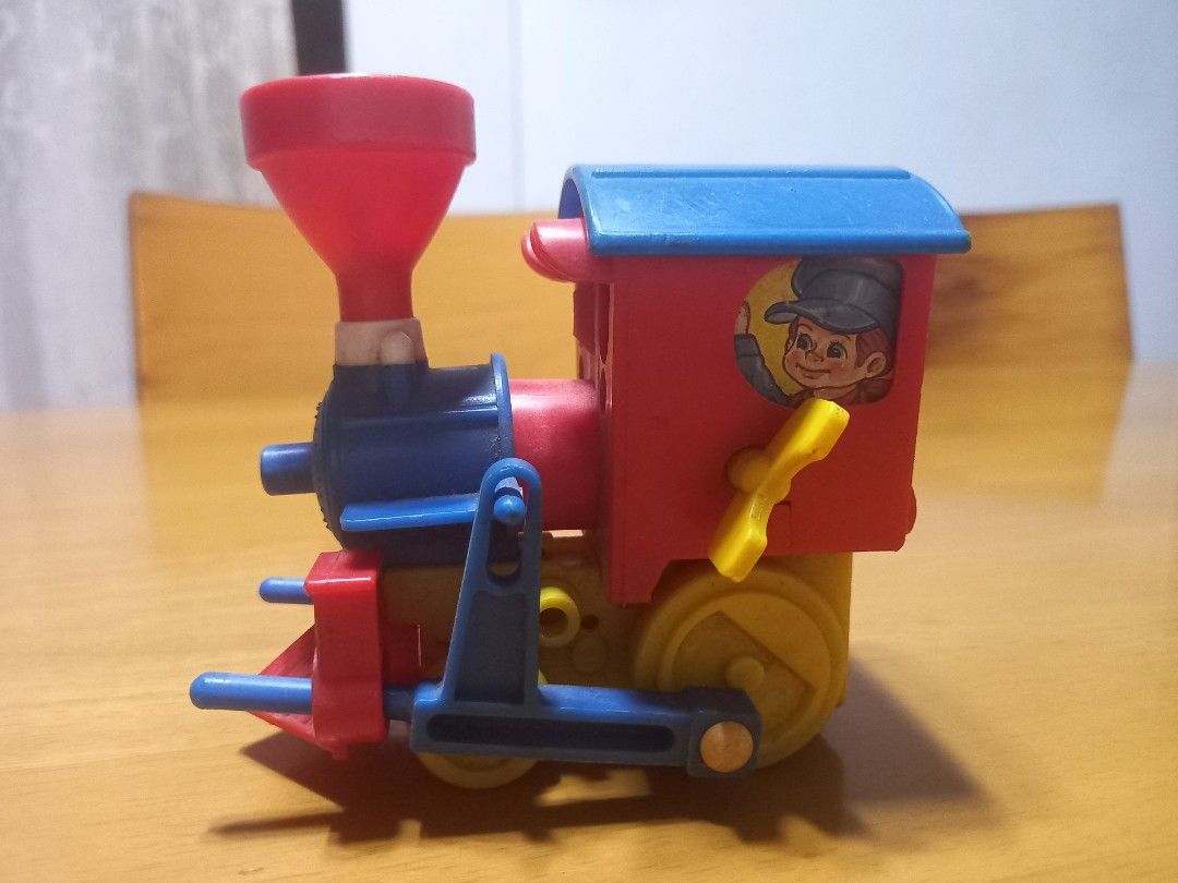 vintage plastic wind-up toy train engine (Category: Kids Toys) located in Manila. Submitted by riaring88 (Listing ID 1464870195, Image 1). Description: - Vibrant design: Red cab, blue roof, yellow wheels, and red funnel chimney - Fun conductor graphic printed on the side window - Perfect for vintage toy collectors - Condition: Good, **wind-up mechanic doesn't function. *** .