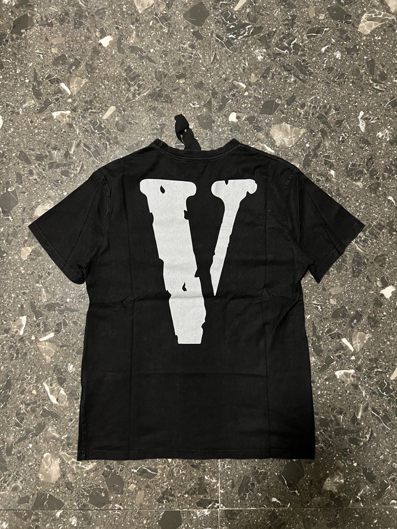 Vlone Black Tee Shirt (Category: Tshirts & Polo Shirts ) located in San Fernando. Submitted by justin_sy (Listing ID 1464887283, Image 2). Description: - Brand: Vlone - Color: Classic Black - Material: 100% Cotton, Made in USA - Size: O - Design: Large chest lettering and iconic 'V' logo on the back - Details: Includes signature hanging neck tag - Condition: Clean overall look with minimal wear on the collar.