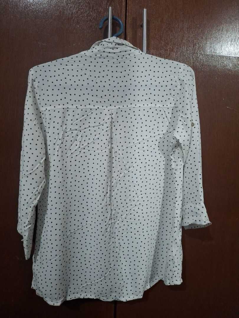 White Button-Up Blouse with Black Square Pattern (Category: Blouses) located in Quezon City. Submitted by 042361 (Listing ID 1464833041, Image 2). Description: - Color/Pattern: White with small black square pattern - Style: Long-sleeve button-up blouse with pointed collar - Features: Front button closure and two buttoned chest pockets - Fabric: Lightweight and comfortable - Fit: Standard fit, regular length - Versatility: Perfect for office wear 