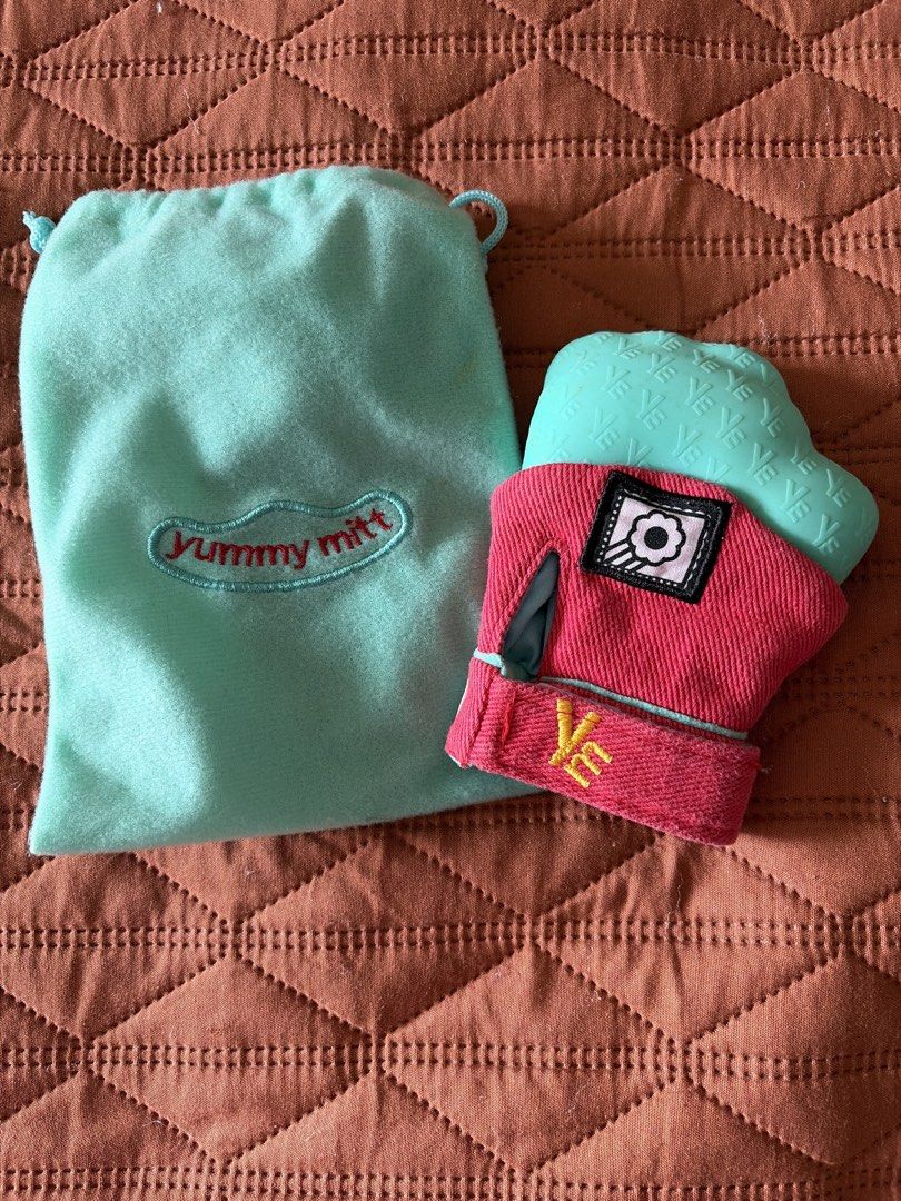 Yummy Mitt Teething Mitten with Storage Pouch (Category: Soothers & Pacifiers) located in San Juan City. Submitted by pea_17 (Listing ID 1464816940, Image 1). Description: - Product: Yummy Mitt Teething Mitten - Color/Design: Red fabric base with adjustable velcro strap and embroidered logo - Material: Textured silicone top to soothe baby's sore gums - Inclusion: Comes with a matching light green drawstring storage pouch - Condition: Clean and re