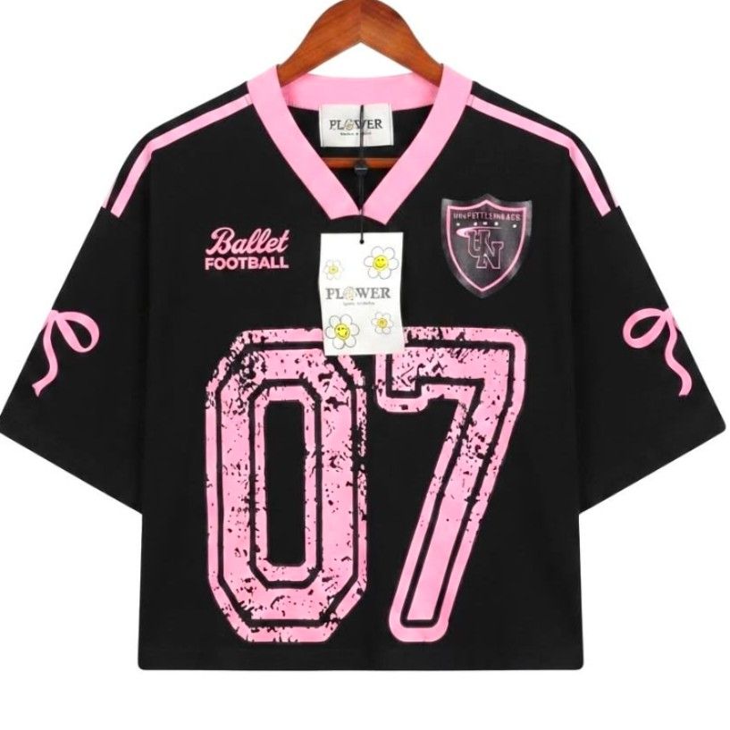 Varsity semi crop Bangkok Shirts (Category: Shirts) located in Quezon City. Submitted by panapton.ph (Listing ID 1459397577, Image 2). Description: -FLASH SALE ONLY 400 -Brandnew Bangkok Tops -Actual item post -Size fit 34 to 44bust -Branding and Origin: Includes a brand tag and hang tag reading "FLOWER" with a smiley face flower motif, indicating it is "Made in Korea". -Design and Details: Black short-sleeve jersey with contrasting pink V-neck c
