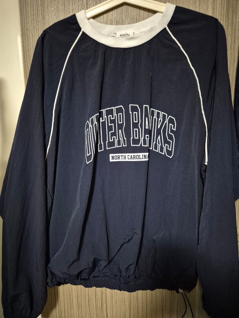 Navy Pullover Jacket (Category: Longsleeves) located in Singapore. Submitted by kaearchives (Listing ID 1459394069, Image 1). Description: - Navy blue lightweight pullover jacket - “Outer Banks, North Carolina” graphic on the front - White ribbed collar and white piping details - Adjustable drawstring hem for a customizable fit - Windbreaker material.