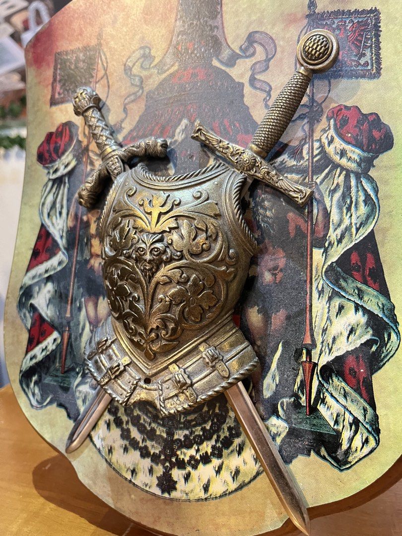 Vintage Medieval Style Heraldic Shield Wall Plaque (Category: Wall Decor) located in Calamba. Submitted by chebvintagedepot (Listing ID 1459335525, Image 3). Description: [B04-03] This vintage medieval-style wall plaque features a decorative miniature metal breastplate and two crossed display swords mounted on a shield-shaped wooden backing. The shield features a printed royal heraldic design with figures, imperial crowns, and heraldic flags. The