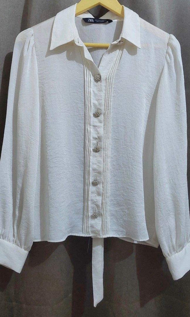 Zara White Puff Sleeve Bow Blouse (Category: Blouses) located in Makati City. Submitted by heinzly (Listing ID 1458545349, Image 2). Description: - White Zara Blouse - Size: Medium (M) - Features: Puff sleeves, bow detail at the neck, pearl-like buttons down the front - Origin: Made in Morocco - Condition: Only worn once.
