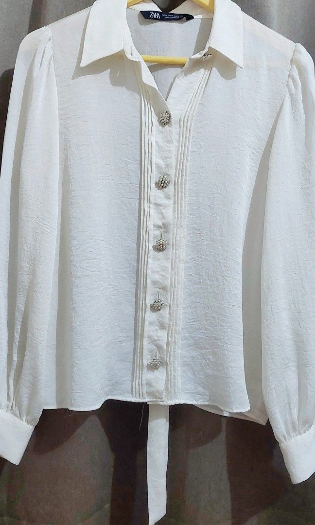Zara White Puff Sleeve Bow Blouse (Category: Blouses) located in Makati City. Submitted by heinzly (Listing ID 1458545349, Image 3). Description: - White Zara Blouse - Size: Medium (M) - Features: Puff sleeves, bow detail at the neck, pearl-like buttons down the front - Origin: Made in Morocco - Condition: Only worn once.