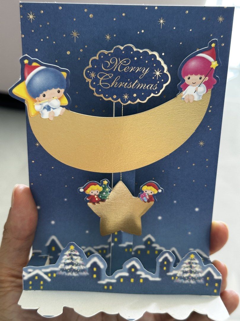 1999年 Sanrio Little Twin Stars 立體聖誕卡 Christmas Pop-Up Card （分類：動漫角色周邊）位於 Hong Kong。 由 tinydings 提交（商品編號 1465034885，圖片 2）。簡介： Sanrio Little Twin Stars Christmas pop-up greeting card from 1999. Blue night sky design with a gold moon, hanging star, and snowy village below. Unused item complete with original protective plastic sleeve and white envelope. Licensed Sanrio item with barcode and copyright text on the back.。
