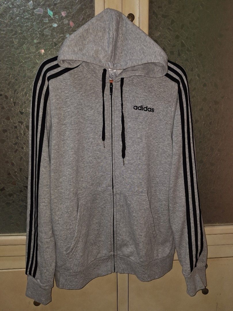 Adidas Grey Zip-Up Hoodie (Category: Hoodies) located in Mabalacat. Submitted by jhaycore05 (Listing ID 1465097558, Image 1). Description: - Brand: Adidas - Color: Grey with black signature stripes and drawstrings - Size: (USA S/M) 20x27.5 - Material: Comfortable cotton - Features: Full zip-up, front kangaroo pockets, and small printed chest wordmark logo - Condition: Excellent no issue.