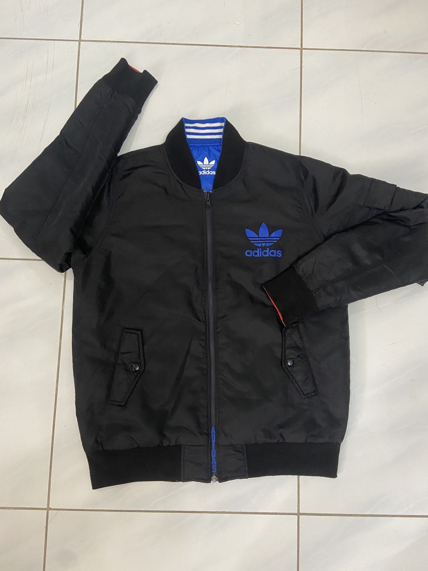 Adidas Reversible Bomber Jacket Black and Blue (Category: Coats, Jackets and Outerwear) located in Pilar. Submitted by romeoabejo54125 (Listing ID 1464983964, Image 1). Description: - Brand: Adidas - Style: Reversible bomber jacket - Side A: Solid black with blue logo hits on chest and back - Side B: Vibrant blue and orange color block with bold arm graphics - Details: Ribbed collar, cuffs, and hem with full zip closure - Condition: Excellent / P