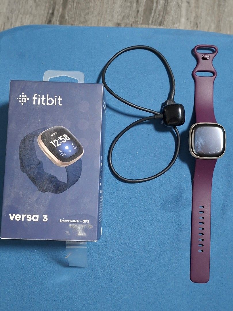 Authentic Fitbit Versa 3 (Category: Wearables & Smart Watches) located in Paranaque City. Submitted by tabsi76 (Listing ID 1465093192, Image 1). Description: - Brand: Fitbit (Authentic) - Model: Versa 3 - Color: Gold case with Purple strap - Inclusions: Original box and charging cable - Condition: Pre-owned, shows minor wear/scratches on the side casing, fully functional - Features: Built-in GPS, heart rate monitor, fitness and health tracking - 