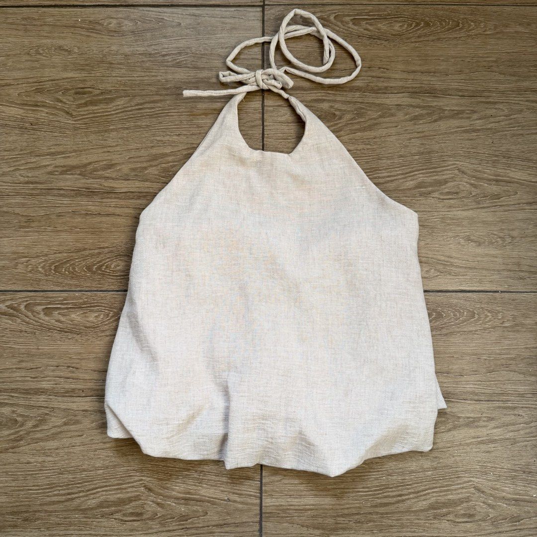 Beige Linen Halter Top Backless Tie Neck Blouse (Category: Sleeveless) located in Cainta. Submitted by nicsboo (Listing ID 1465087707, Image 1). Description: - Material: Breathable linen-blend fabric in a neutral beige earth tone - Design: Halter neckline with an adjustable tie closure and open back - Fit: Flattering flared bubble hem at the bottom - Styling: Easy to pair with high-waisted shorts, skirts, or denim - Condition: Perfect basic piece