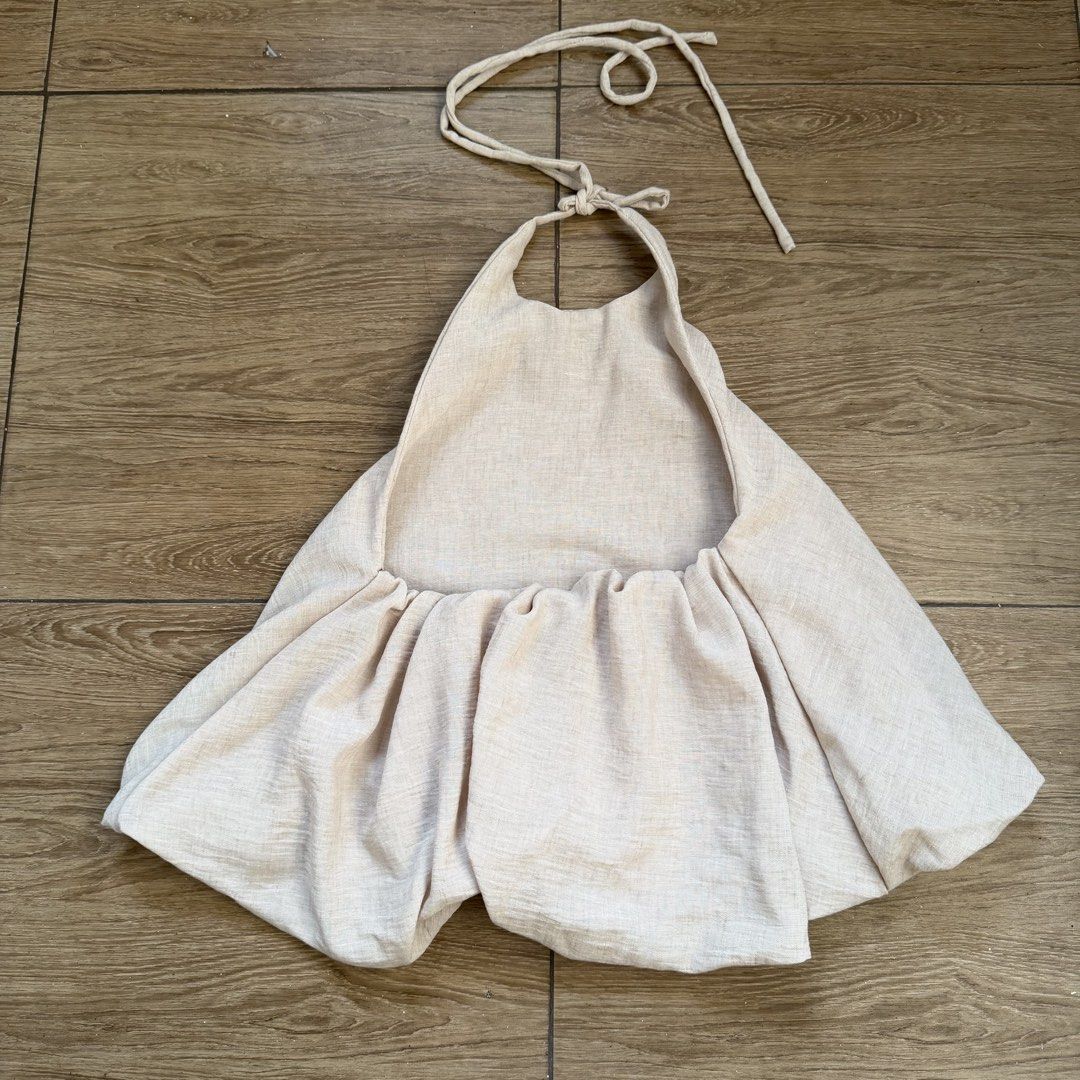 Beige Linen Halter Top Backless Tie Neck Blouse (Category: Sleeveless) located in Cainta. Submitted by nicsboo (Listing ID 1465087707, Image 2). Description: - Material: Breathable linen-blend fabric in a neutral beige earth tone - Design: Halter neckline with an adjustable tie closure and open back - Fit: Flattering flared bubble hem at the bottom - Styling: Easy to pair with high-waisted shorts, skirts, or denim - Condition: Perfect basic piece