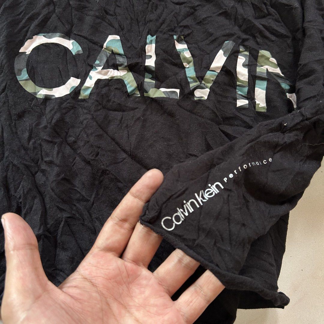 Calvin Klein Black Camo Crop Top 😍 (Category: Shirts) located in Jinoba-an. Submitted by eegiboy (Listing ID 1465001758, Image 3). Description: - Brand: Calvin Klein Performance - Size: S (Brand new with tags attached!) - Design: Bold green and white camo print spelling out 'CALVIN' across the chest - Details: Short sleeves, ribbed neckline, and small white logo near the sleeve cuff - Material: 60% cotton, 40% modal (super soft and breathable) -