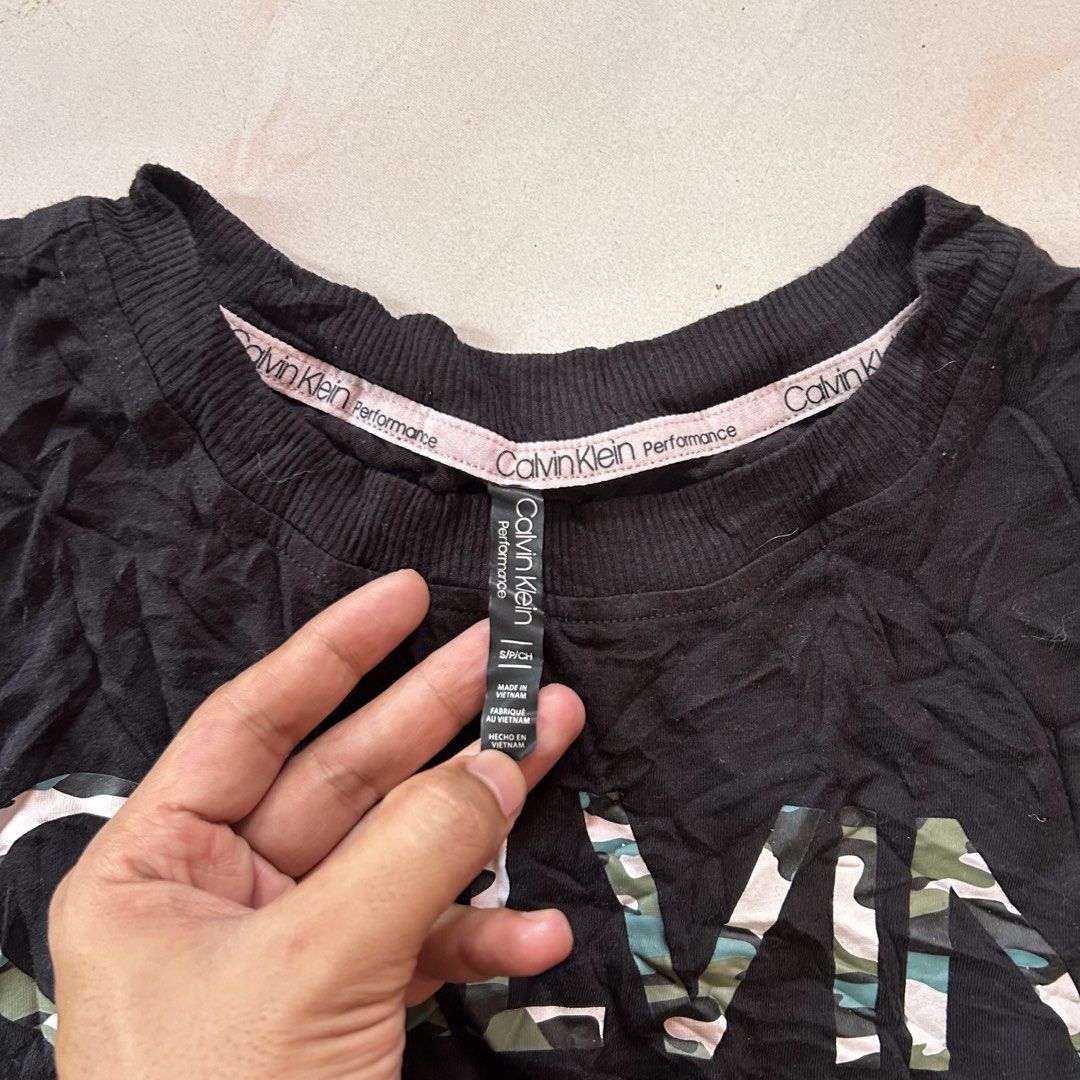 Calvin Klein Black Camo Crop Top 😍 (Category: Shirts) located in Jinoba-an. Submitted by eegiboy (Listing ID 1465001758, Image 2). Description: - Brand: Calvin Klein Performance - Size: S (Brand new with tags attached!) - Design: Bold green and white camo print spelling out 'CALVIN' across the chest - Details: Short sleeves, ribbed neckline, and small white logo near the sleeve cuff - Material: 60% cotton, 40% modal (super soft and breathable) -