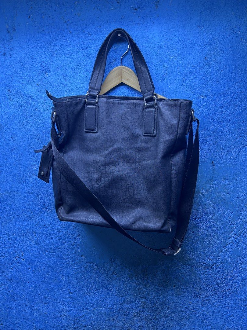 Calvin Klein Monogram Tote Bag with Shoulder Strap (Category: Tote Bags) located in Quezon City. Submitted by thriftxgoods (Listing ID 1465078455, Image 1). Description: Calvin Klein tote bag in dark blue canvas with all-over monogram pattern. Includes dual top handles plus a detachable adjustable crossbody strap. Zipper top closure keeps your items secure. Inside lining shows discoloration near the opening rim, plus an inner zippered pocket with
