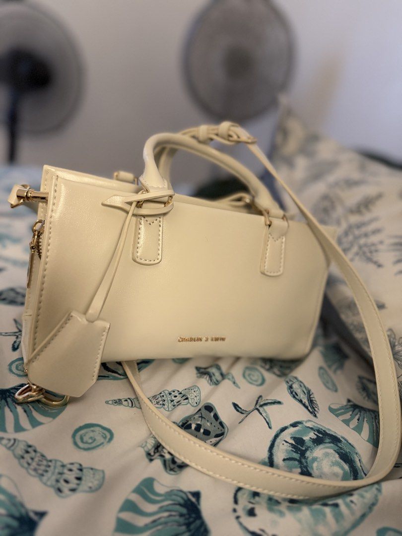 Charles & Keith Kerry Handbag with Strap (Category: Shoulder Bags) located in Rizal. Submitted by clrss_dclttr (Listing ID 1465135985, Image 1). Description: Charles & Keith off-white handbag. Off white to, due to my light kaya iba color. RFS: Decluttering, super bago pa nito. Badly need to declutter things, get niyo na tooo 🥹 Smooth faux leather structure with gold-tone hardware branding on the front. Includes matching top handles plus an adjus